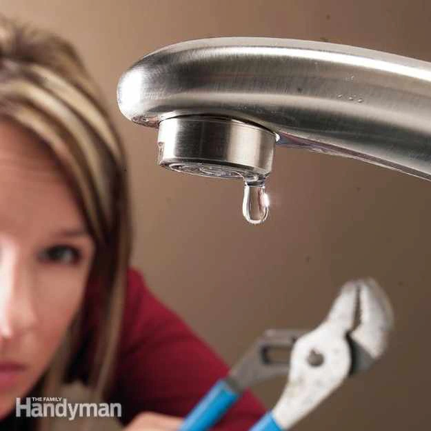 female DIY home owner holding a pair of adjustable pliers slightly out of focusing looking at a leaky faucet.