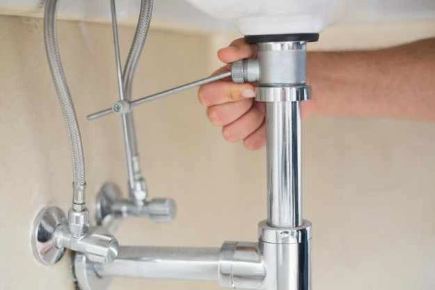 plumbing repair man holding a drain plug fixture underneath of a sink.
